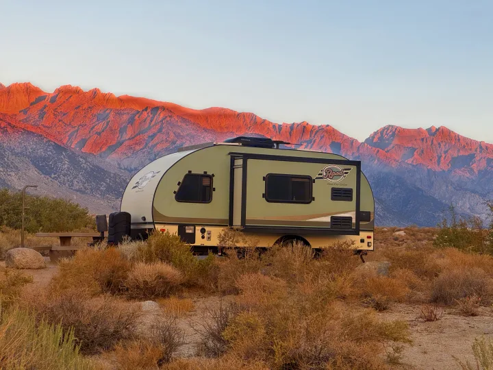 An R-Pod RV rental is parked in a desert campsite, with majestic mountains glowing red from the sunset in the background.. R-Pod Hood River Edition 2015