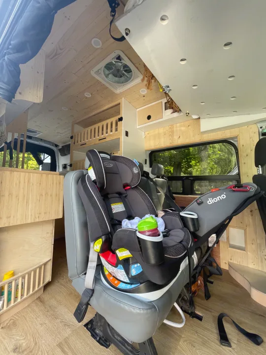 RV rental interior showing Graco and Diono child safety seats installed in a wood-paneled camper van, ready for family travel.. Ford Transit 2019