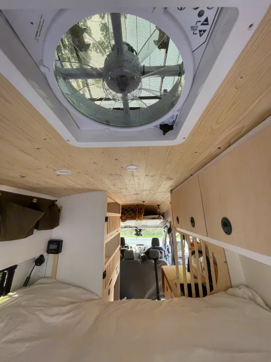 Cozy RV rental camper van interior: wooden ceiling, roof fan, bed, and storage visible towards the driver's cab.. Ford Transit 2019