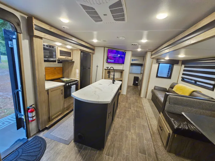 Bright RV rental: full kitchen with island, living room with sofa, TV, wood floors & modern amenities visible.. Forest River Cherokee Alpha Wolf 2021