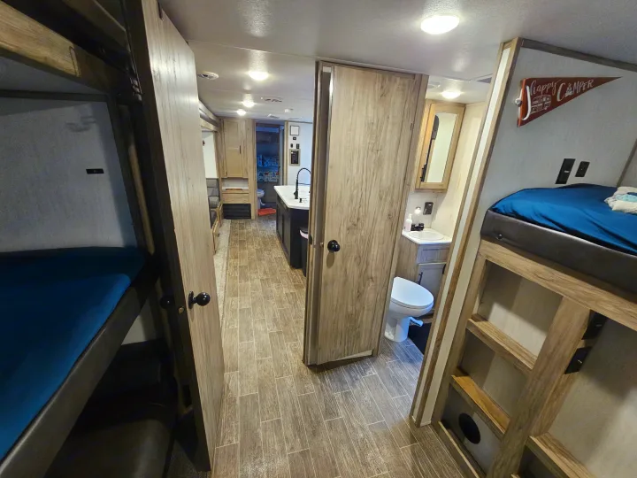 Spacious rv rental interior featuring bunk beds, a central hallway leading to a kitchen, and a visible bathroom on the right.. Forest River Cherokee Alpha Wolf 2021