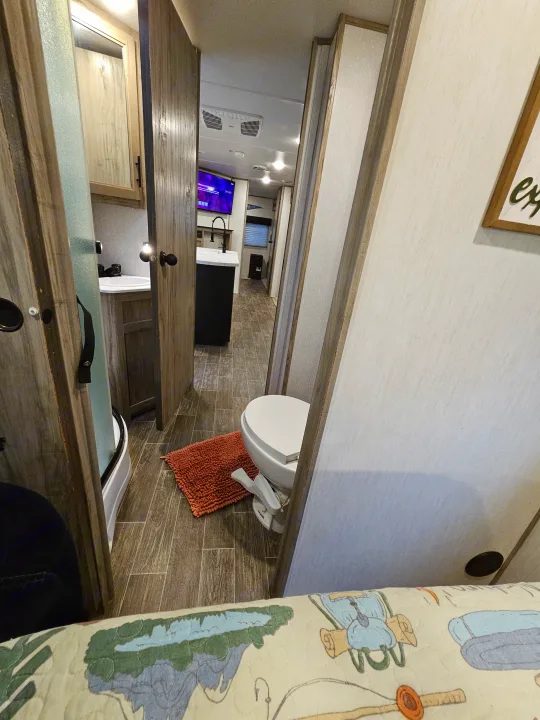 Explore a modern RV rental interior: bathroom with toilet & shower, leading to a functional living space with kitchen and TV.. Forest River Cherokee Alpha Wolf 2021