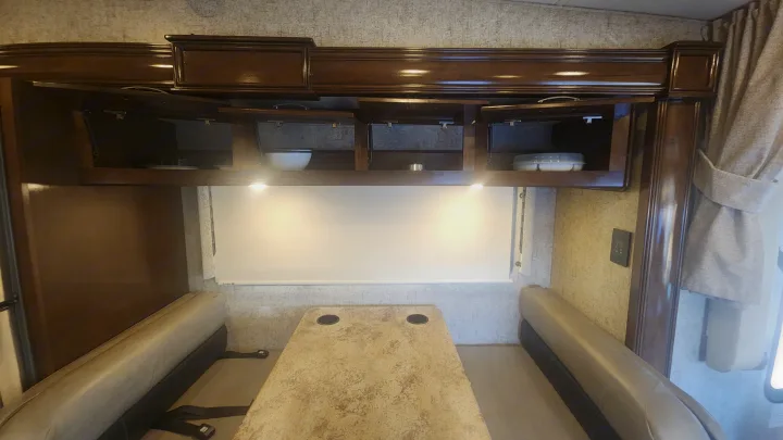 RV rental dinette area with built-in seating, table with cupholders, and accessible overhead cabinets. Cozy travel space.. Thor Outlaw 2017