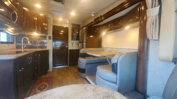 Spacious RV rental interior showcasing a modern kitchen with dark wood cabinetry, a comfortable dinette, and bright overhead lighting.. Thor Outlaw 2017