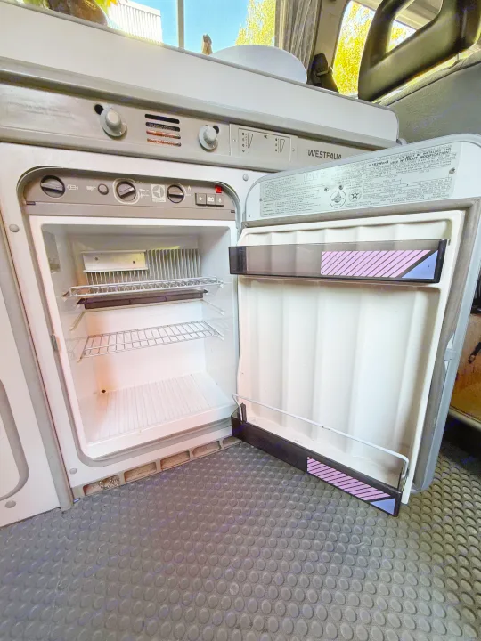 Inside an RV rental, a Dometic Westfalia camper fridge with its door open, revealing shelves and operating controls.. Volkswagen T3 Westfalia 1991