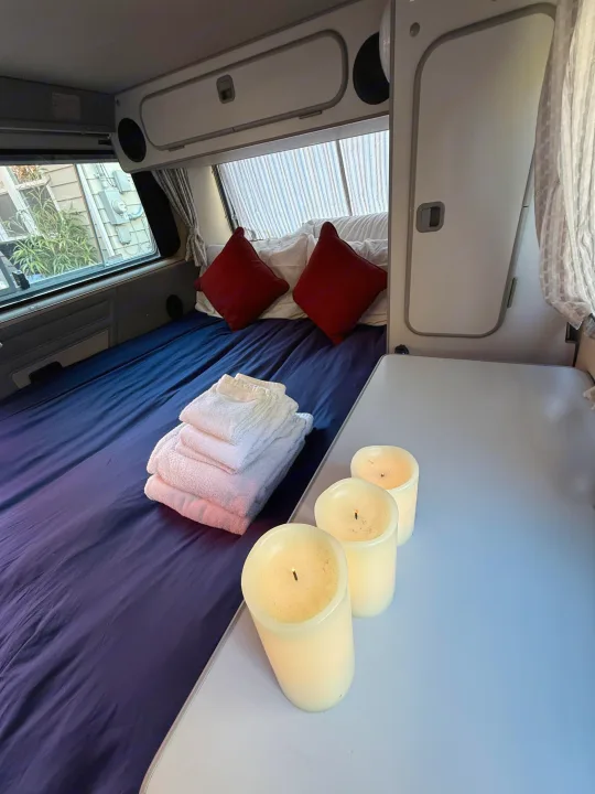 Relax in comfort! RV rental interior with a neatly made bed, fresh towels, and decorative candles on the table.. Volkswagen T3 Westfalia 1991