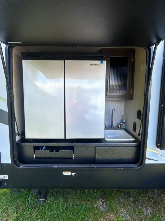 This RV rental's convenient outdoor kitchen, equipped with a refrigerator, sink, and storage, visible in this open compartment.. Escape Trailer Alpha Wolf 2020