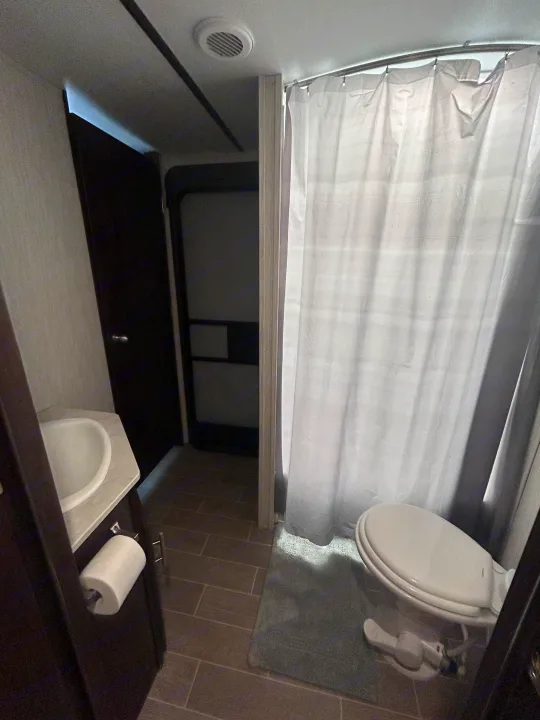 Compact RV rental bathroom showing sink, toilet with bidet, and shower curtain. Features tiled flooring and a ceiling vent.. Escape Trailer Alpha Wolf 2020