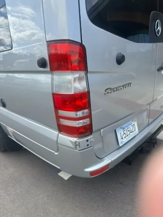 Rear of a silver Mercedes Sprinter RV rental, showing its left taillight, bumper, and Montana license plate.. Coachmen Galleria 2020