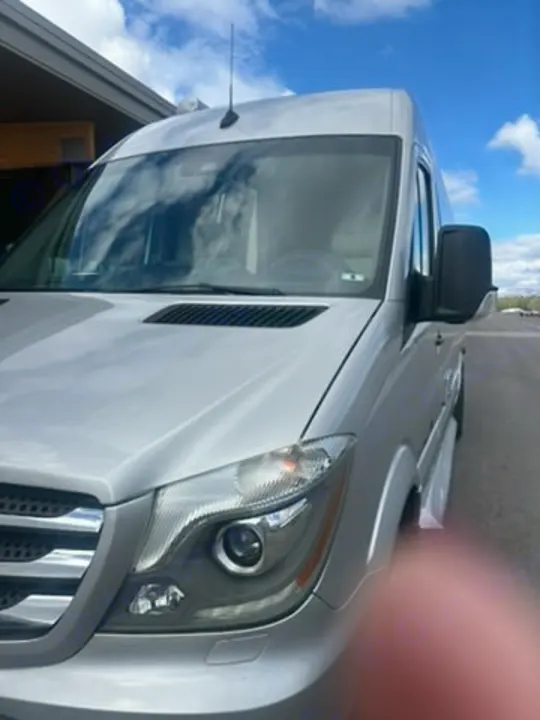 Silver Mercedes Sprinter van, a versatile rv rental. Blue sky reflects in windshield; blurry finger obscures lower right.. Coachmen Galleria 2020