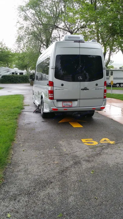 Silver Mercedes Sprinter RV rental parked at campsite 54, with other RVs and trees in the background.. Coachmen Galleria 2020
