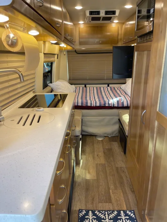 Enjoy this rv rental's bright interior: compact kitchen with cooktop, sink, microwave, cozy bed with striped duvet, and wood cabinets.. Coachmen Galleria 2020