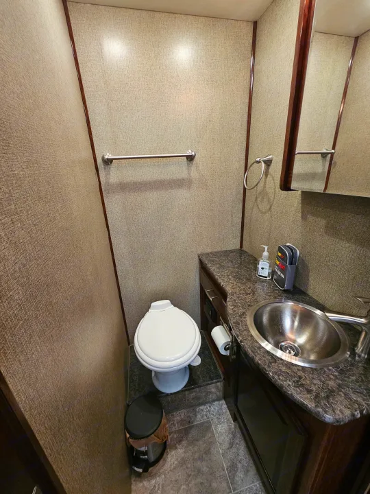 This functional RV rental bathroom features a toilet, sink, vanity, mirror, and towel racks, all in neutral tones.. Holiday Rambler Vesta 2018