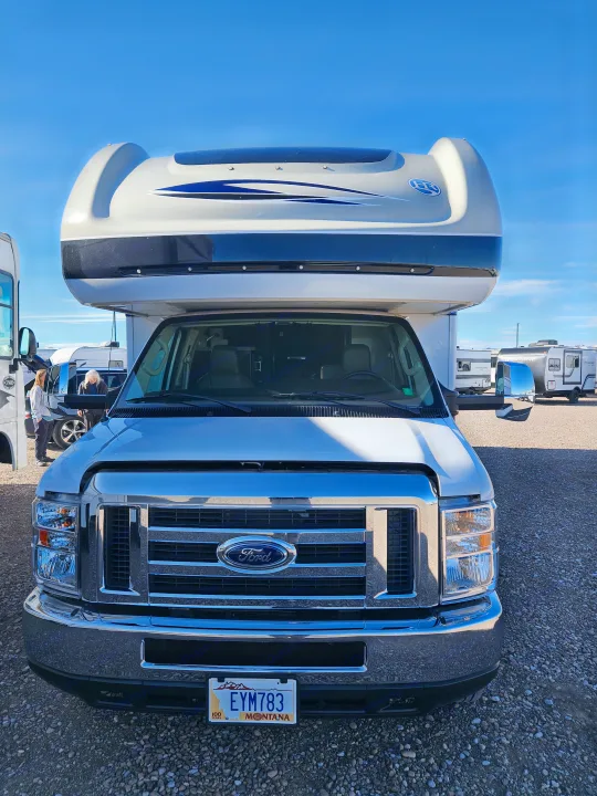 Front view of a white Ford RV rental parked on a gravel lot under a clear blue sky. A Montana license plate is visible.. Holiday Rambler Vesta 2018