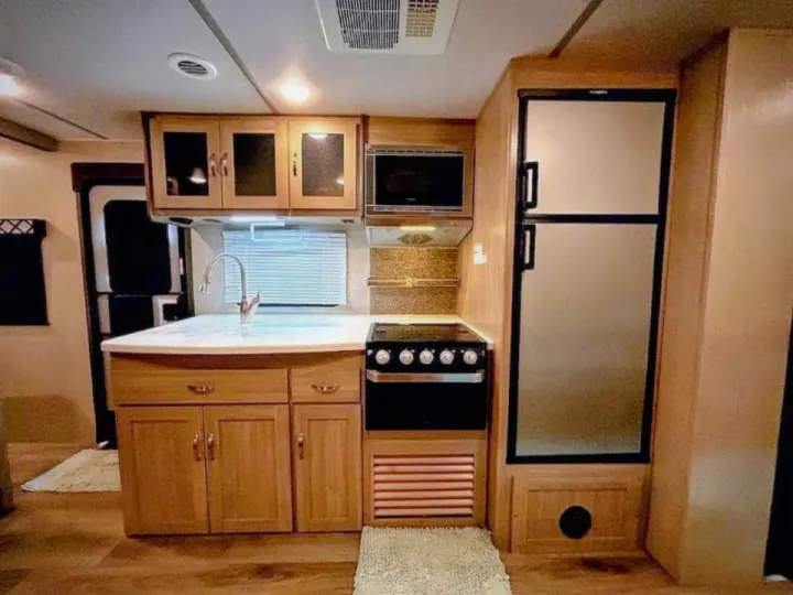 Inside an RV rental: a modern kitchen with light wood cabinets, a full-size refrigerator, stove, microwave, and sink.. Coachmen Other 2020