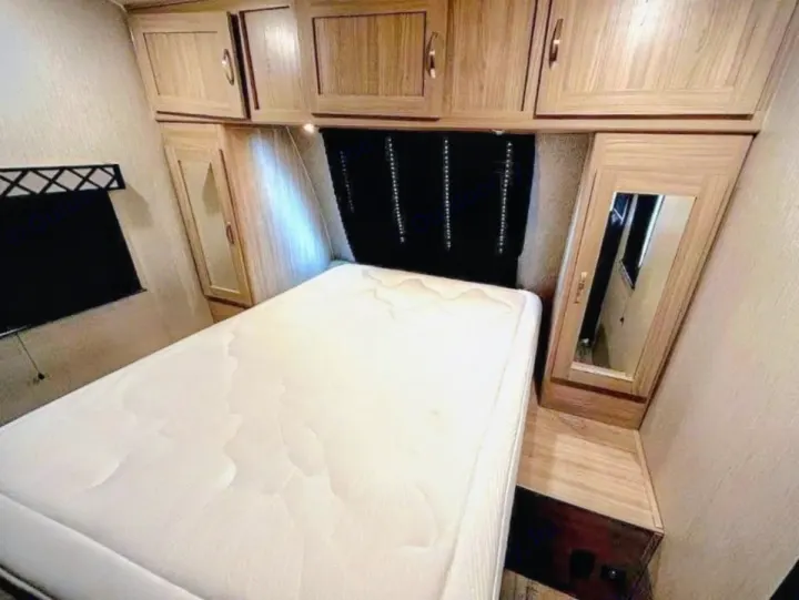 Cozy RV rental bedroom featuring a plush white mattress, wooden overhead and bedside cabinets, and a mirror.. Coachmen Other 2020