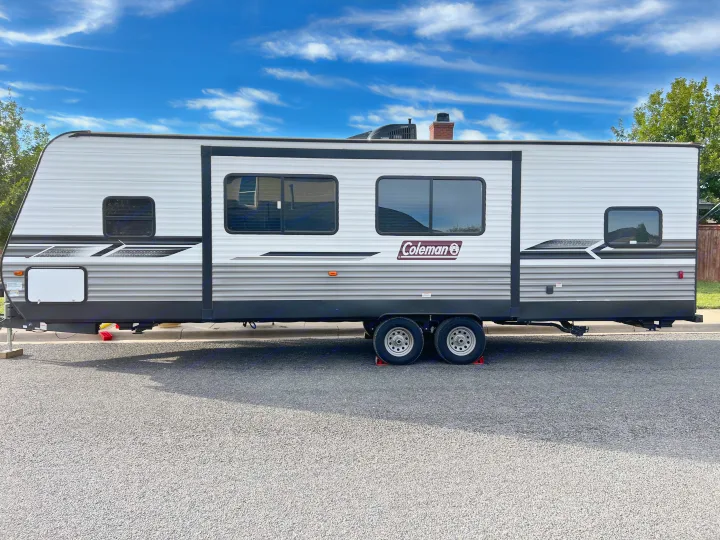 This Coleman travel trailer RV rental, with its white and gray exterior and dual axles, is parked on asphalt under a blue sky.. Dutchmen Coleman Lantern 2022