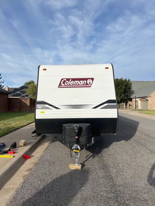 Front view of a Coleman travel trailer, ideal for an RV rental, parked on a residential street with leveling equipment.. Dutchmen Coleman Lantern 2022