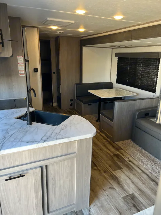 Clean RV rental interior featuring a kitchen, dining booth with black cushions, and light wood cabinetry over wood-look flooring.. Dutchmen Coleman Lantern 2022