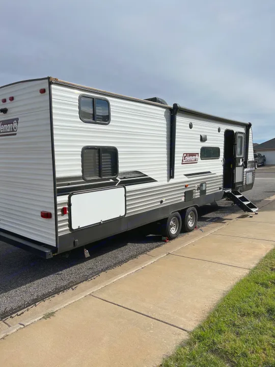 This white Coleman travel trailer RV rental is parked on a gravel driveway with steps extended, ready for adventure.. Dutchmen Coleman Lantern 2022