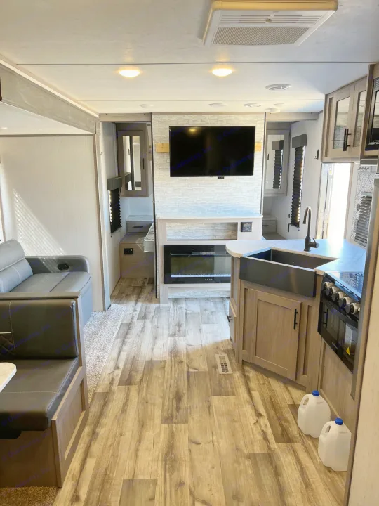 Modern RV rental interior with a cozy living area, kitchen, and electric fireplace. Features sleek design & wood-look flooring.. Dutchmen Coleman Lantern 2022
