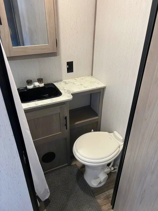 Experience comfort in this RV rental's compact bathroom, featuring a black sink, marble-look counter, and white toilet.. Dutchmen Coleman Lantern 2022