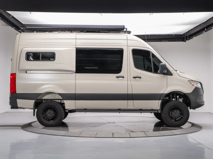 Side profile of a beige off-road camper van with a roof awning, chunky tires, and custom suspension, available for rv rental.. MERCEDES-BENZ Sprinter 2500 AWD 2024