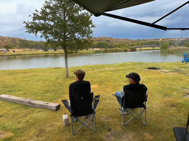 Two people in chairs enjoying a tranquil lake view from an RV rental campsite, surrounded by nature and hills.. Grand Dessing Transend 2025