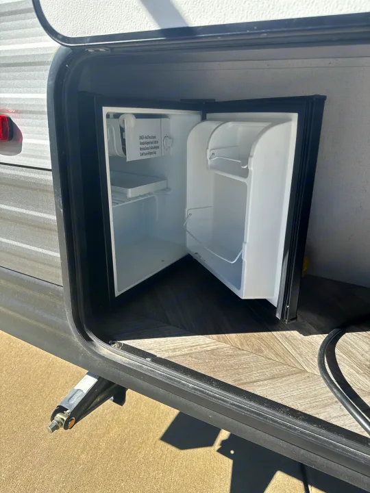 An open, empty mini-fridge in an RV rental's outdoor kitchen compartment, ready for your camping provisions.. Forest River Salem FSX 2022