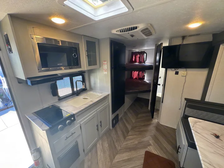 Modern **rv rental** showing kitchen (microwave, stove, sink), bunk beds, dining area, and TV. Light-filled camper space.. Forest River Salem FSX 2022