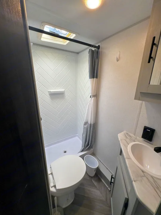 This RV rental bathroom features a compact shower, toilet, and modern vanity with a sink.. Forest River Salem FSX 2022