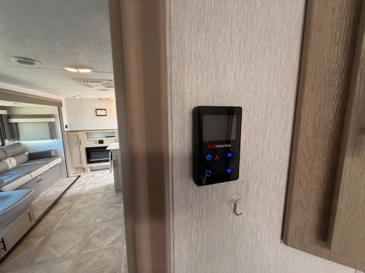 Digital climate control panel in an RV rental, with a view of the living area, sofa, and electric fireplace in the background.. Forest River Wildwood X-Lite Platinum 2024