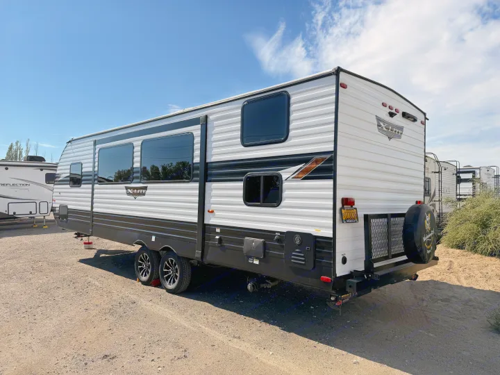 Explore this spacious 'X-LITE' travel trailer, perfect for your next rv rental adventure. White with black trim, parked on gravel.. Forest River Wildwood X-Lite Platinum 2024