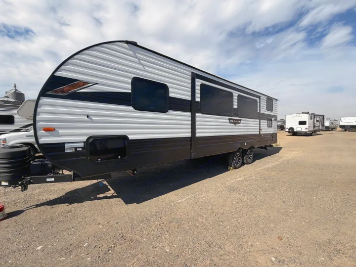 Sleek black and white travel trailer, perfect for an rv rental, parked on a gravel lot under a partly cloudy sky.. Forest River Wildwood X-Lite Platinum 2024