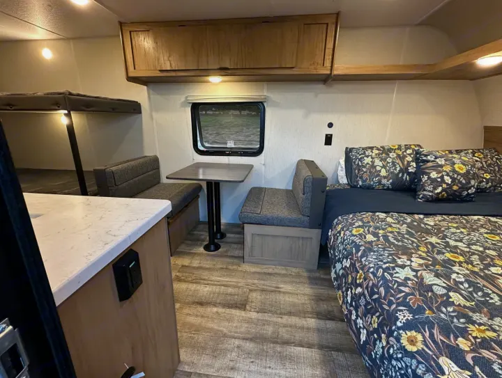 Interior of an rv rental with a bed, dinette, bunk beds, and overhead storage. Features floral bedding and wood accents.. Forest River Cherokee Wolf Den 16 EV 2024