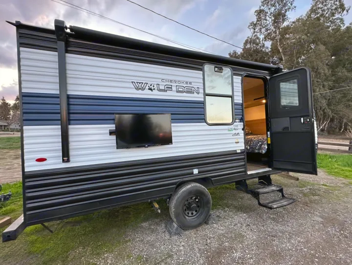 Wolf Den RV rental: a stylish striped travel trailer with outdoor TV and open door revealing a cozy interior, ready for camping.. Forest River Cherokee Wolf Den 16 EV 2024