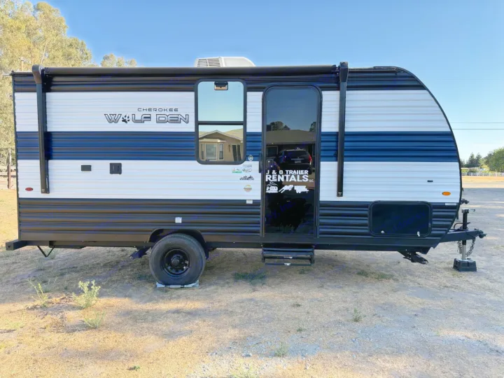 A parked black, white, and blue Cherokee Wolf Den travel trailer, identified as an RV rental from J & G Trailer Rentals.. Forest River Cherokee Wolf Den 16 EV 2024