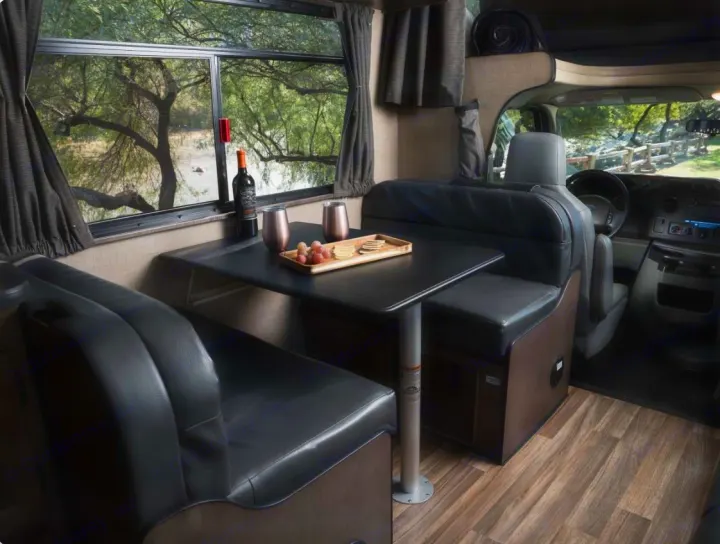 This cozy rv rental features a dinette with black leather seating, a table with wine and snacks, and a scenic window view.. Thor Majestic 2019