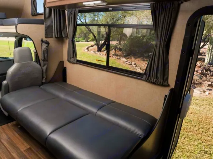 Spacious RV rental interior with a comfy black sleeper sofa, large window views, and driver's seat visible. Perfect for road trips.. Thor Majestic 2019