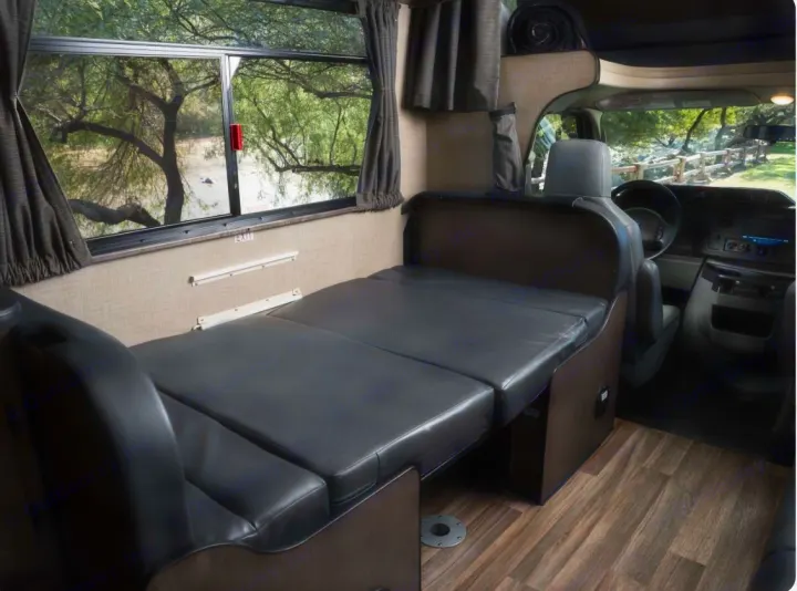 Inside an **rv rental**: a flexible bed/seating area with a large window overlooking nature, leading to the cockpit.. Thor Majestic 2019