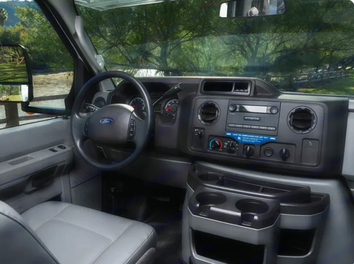 Inside an RV rental, the spacious Ford van dashboard features a steering wheel, radio, and cup holders for travel.. Thor Majestic 2019