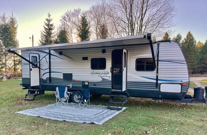 Springdale RV rental ready for adventure: travel trailer with extended awning, chairs, and mat at a peaceful campsite.. Keystone Springdale 2017