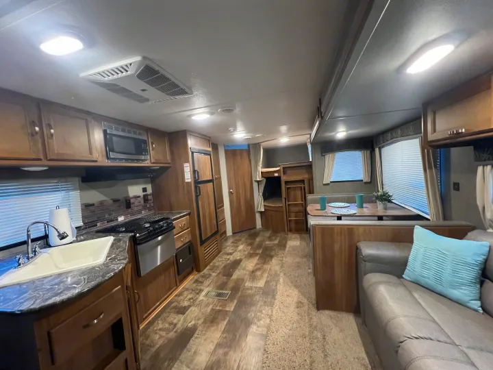Bright RV rental interior showcasing a kitchen, dining area, comfortable sofa, and bunk beds, perfect for travel.. Keystone Springdale 2017