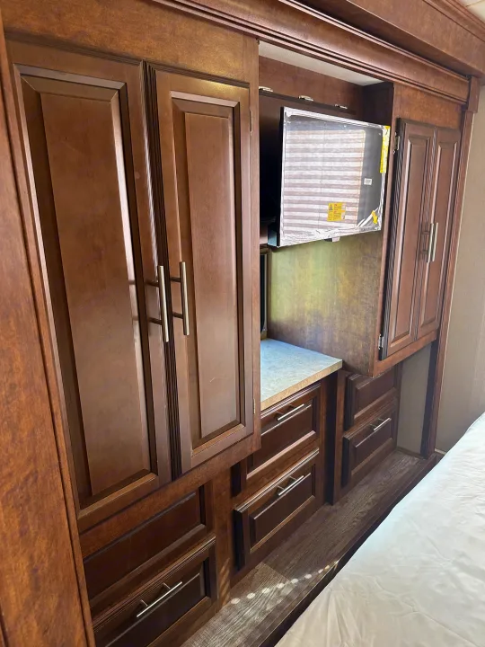 RV rental bedroom with dark wood cabinets, drawers, a recessed TV, and a comfortable bed.. Forest River FR3 2017