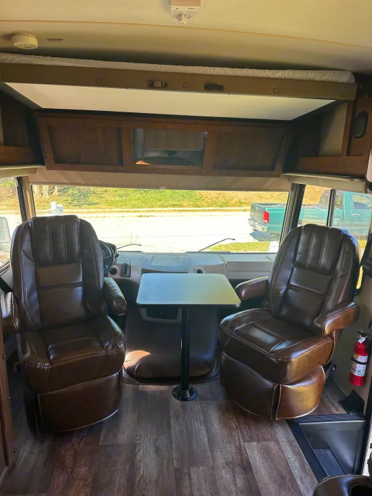 RV rental cabin with two large brown leather captain's chairs, a small table, and an overhead sleeping area.. Forest River FR3 2017