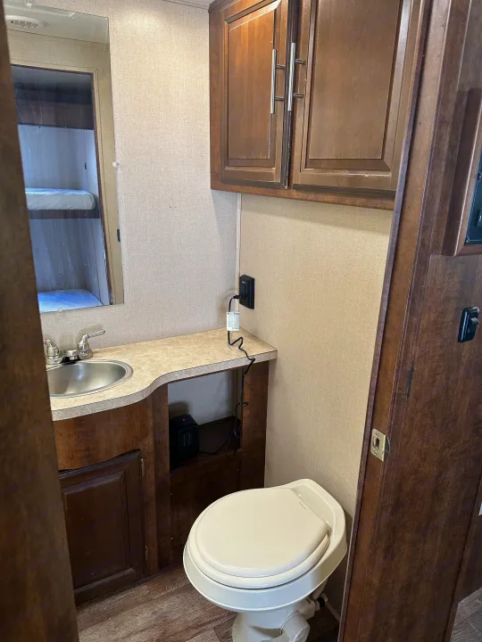 Compact RV rental bathroom with toilet, sink, wood cabinets, and a mirror reflecting bunk beds. A small heater is under the counter.. Forest River FR3 2017