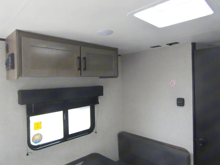 An RV rental's interior features gray overhead cabinets, a window with a dark blind, a skylight, and comfortable dinette seating.. Jayco Jay Flight SLX 2025