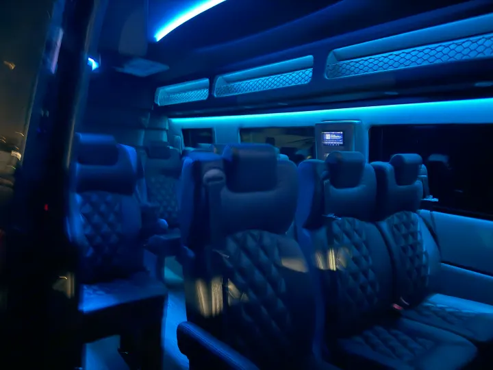 Experience premium comfort in this luxury RV rental interior, featuring ambient blue lighting and plush, quilted seating.. Mercedes 15 Passenger Luxury shuttle 2025