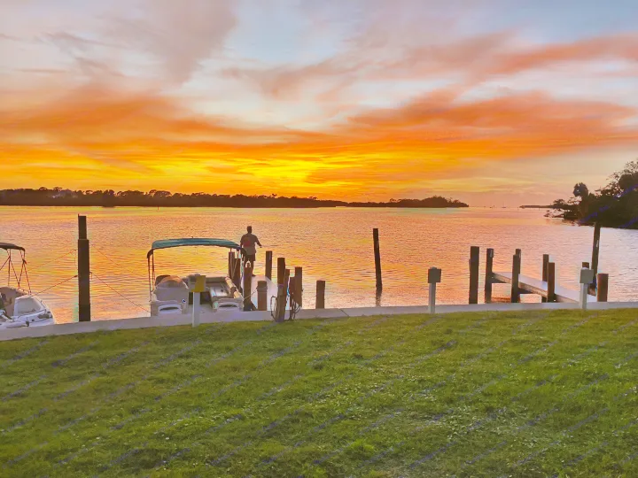 A person on a dock at sunset, next to a boat, with the sky ablaze in orange and red. The perfect end to an RV rental trip.. East to West Entrada 2025