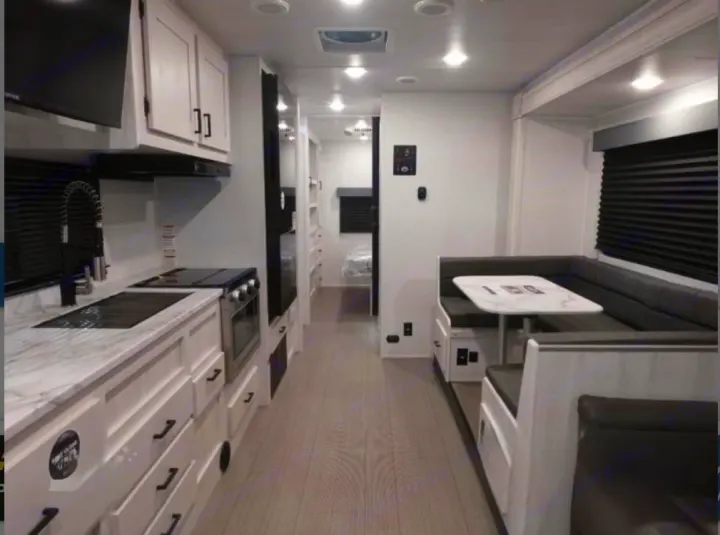 Explore this modern RV rental's bright kitchen, U-shaped dinette, and clean, spacious interior with light wood floors.. East to West Entrada 2025